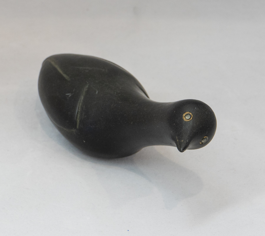 Small dark stone carving of a bird with distinctive eyes.