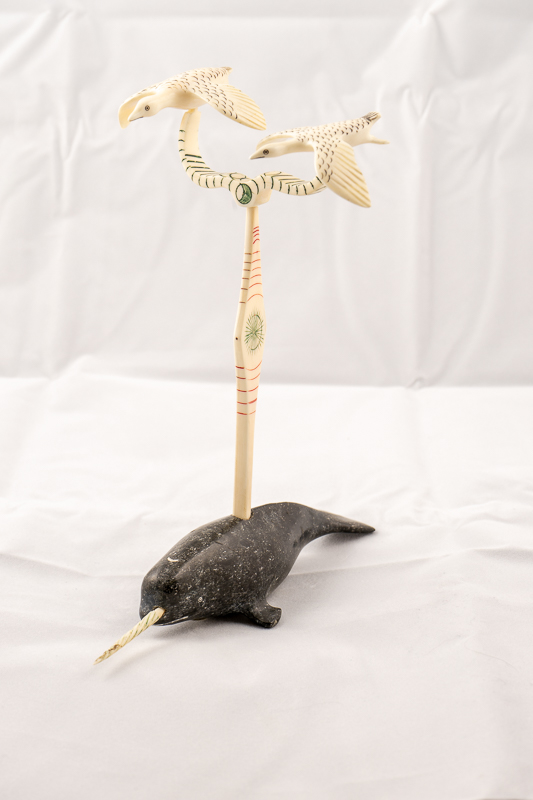 Two ivory birds flying above a stone narwhal with ivory tusk.