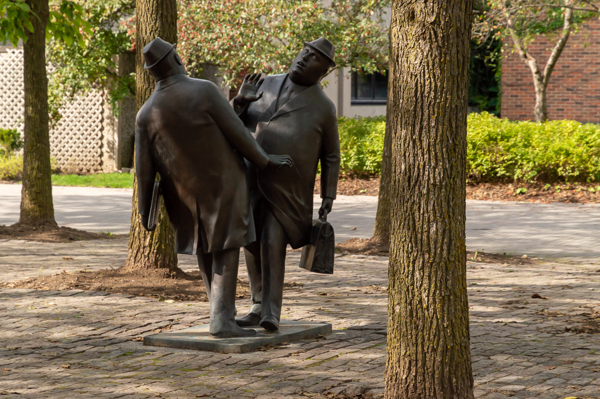 Two heavy-set businessmen in bronze, facing each other in an apparent collision course. 
